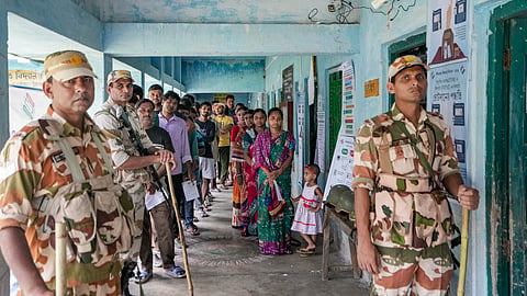 Security personnel stand guard as voters wait in a queue to cast their votes at a polling station during a repoll ordered by the Election Commission following reports of electoral malpractices, at Magrahat Paschim constituency, in South 24 Parganas district, West Bengal, Saturday, May 2, 2026.