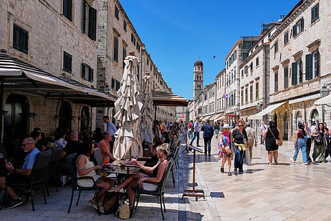 People sit in a cafe as others walk on the main street of Stradun in old town Dubrovnik, Croatia, Monday, April 27, 2026.